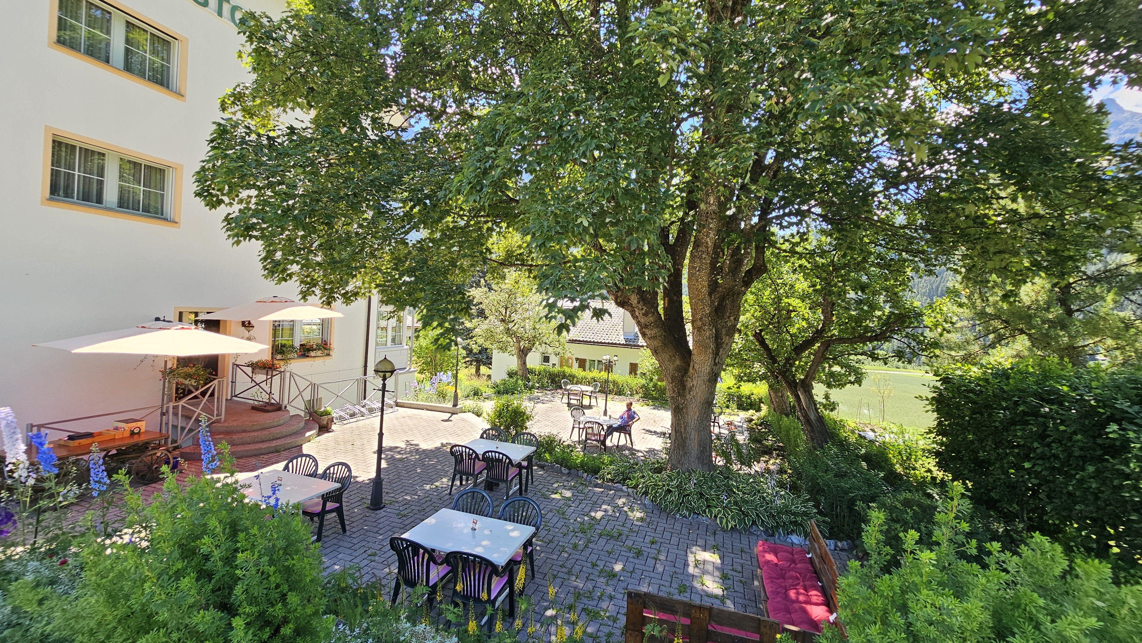 Gartenterrasse - Blumen - Lounge Sofa - Garten Tisch - Garten Stuhl - Sonnenschirm - Mittagmenü - Nachmittag Karte - Bar Karte - Berg Aussischt